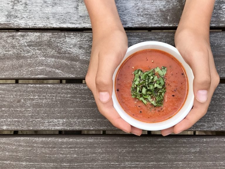 woman holding cup of creamy tomato basil soup